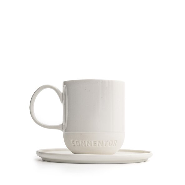 The photo shows a white porcelain coffee mug with saucer. It holds 330 ml and features the SONNENTOR letters..